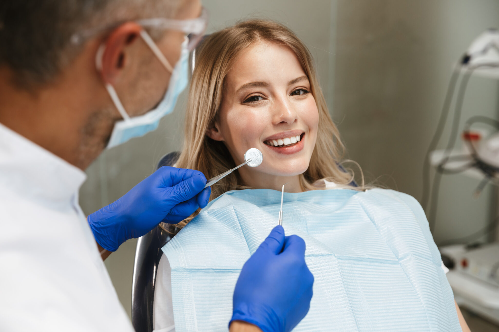 Image of content young woman sitting in dental chair at medical center while professional doctor fixing her teeth
